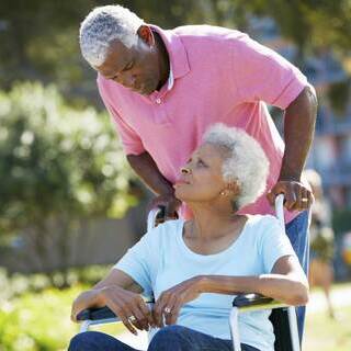 Elderly man in a pink shirt pushing elderly female in a wheelchair